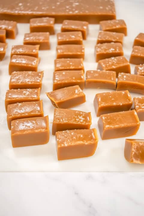 Rectangular pieces of salted caramels are arranged on a sheet of parchment paper, with some sprinkled with sea salt for a delightful gourmet sweets touch.