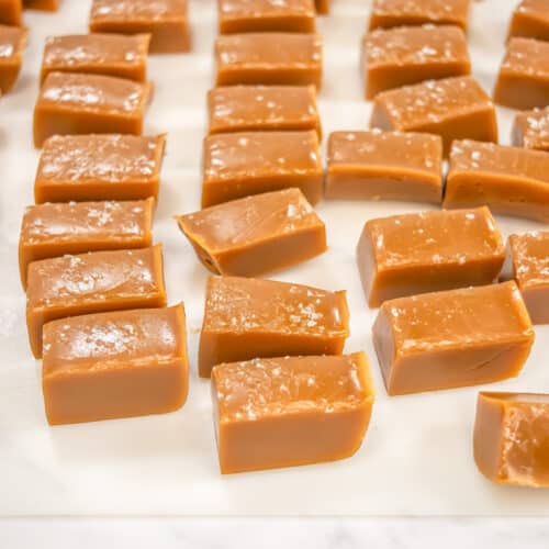 Rectangular pieces of salted caramels are arranged on a sheet of parchment paper, with some sprinkled with sea salt for a delightful gourmet sweets touch.