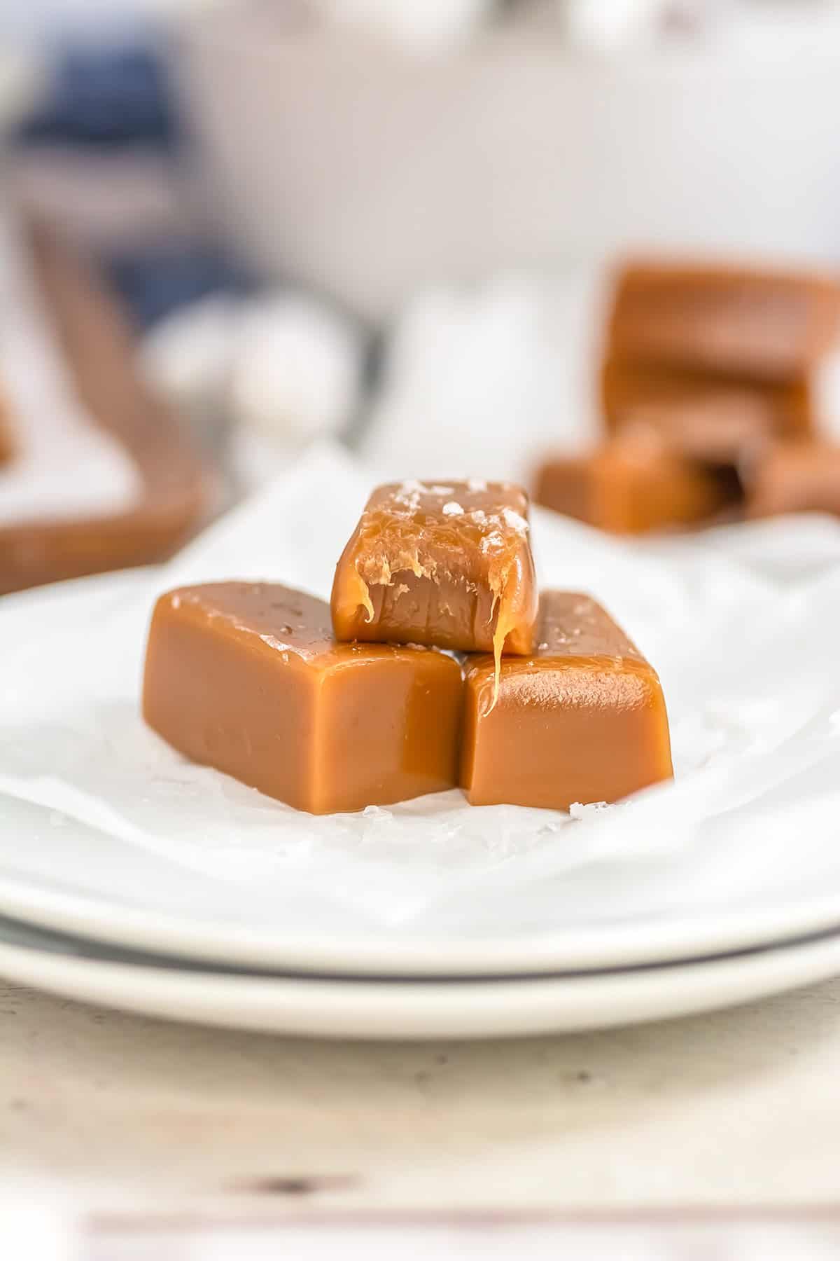 A close-up of three pieces of salted caramels on a white plate, with one piece partially melted and sprinkled with sea salt, showcasing irresistible gourmet sweets.