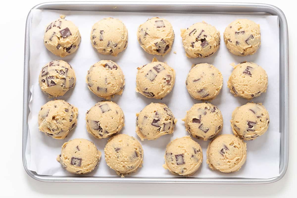 A baking tray lined with parchment paper holds 18 evenly spaced scoops of Levain Bakery-inspired chocolate chip cookie dough.