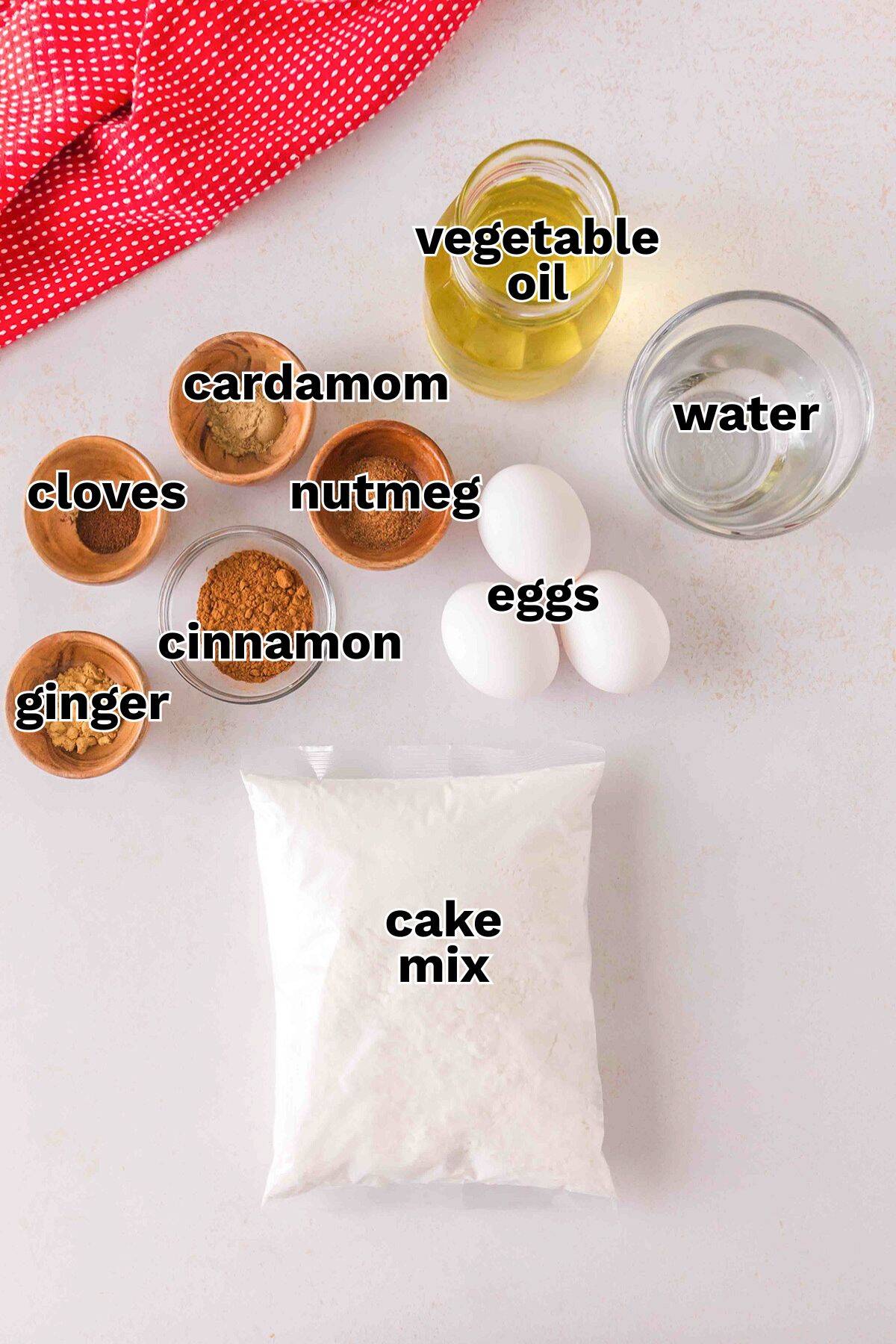 A bag of yellow cake mix, three eggs, a cup of water, oil, and small bowls of cinnamon, ginger, cloves, nutmeg, and cardamom on a countertop—everything you need for how to make spice cake at home.