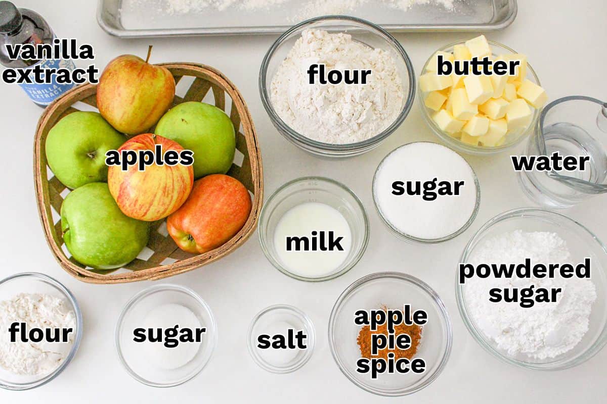 Top-down view of baking ingredients labeled: apples, flour, butter, sugar, powdered sugar, milk, water, salt, apple pie spice, and vanilla extract—perfect for making delicious Apple Pie Bars.