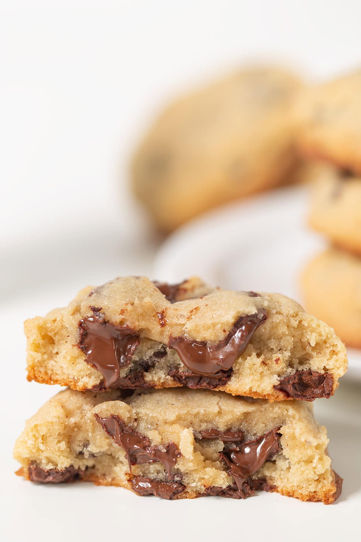 A close-up of two halves of a Levain Bakery chocolate chip cookie stacked together, revealing gooey melted chocolate chips inside. Other cookies are blurred in the background.