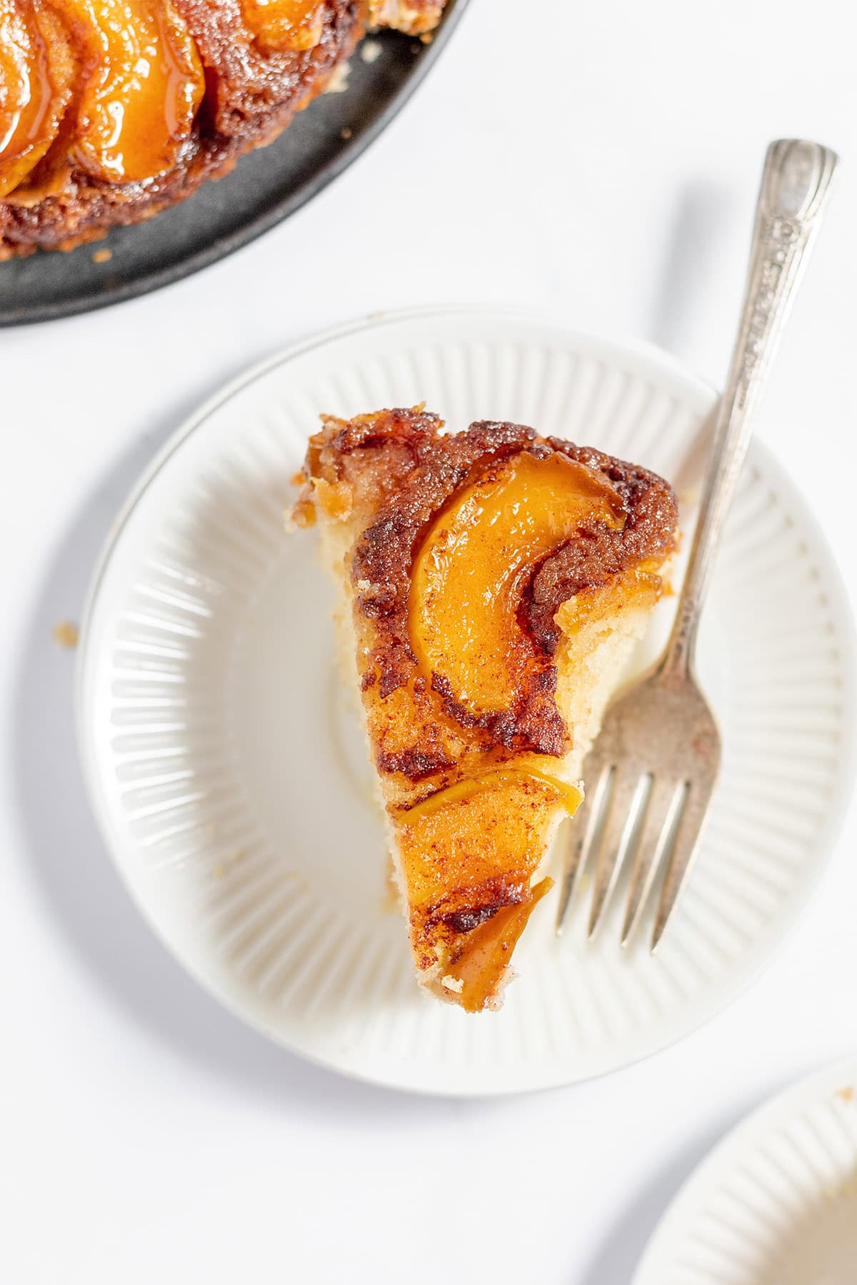 A slice of apple upside-down cake on a white plate with a fork, viewed from above—this dessert is perfect for fans of classics like Apple Upside Down Cake.