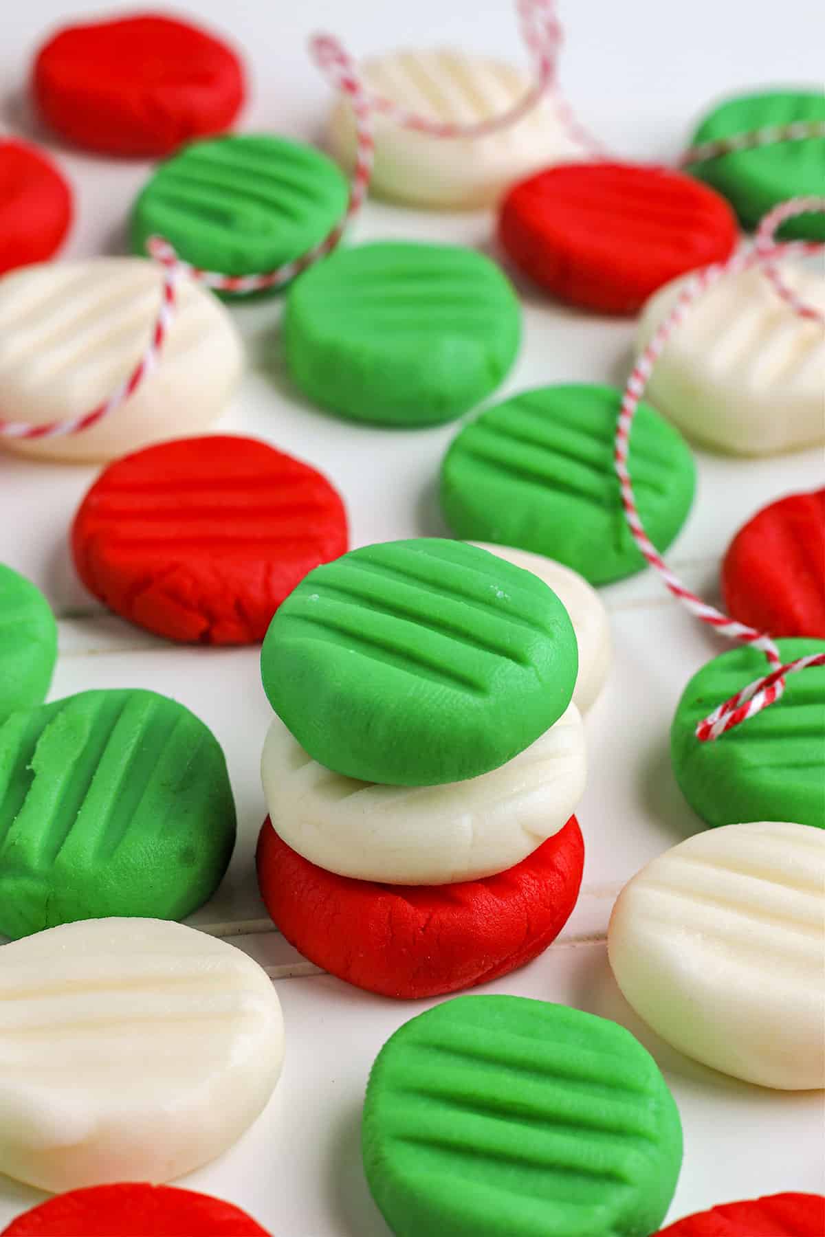 Round red, green, and white Homemade Butter Mints with ridged tops are arranged on a white surface, some stacked and some scattered, with a red and white string woven through them.