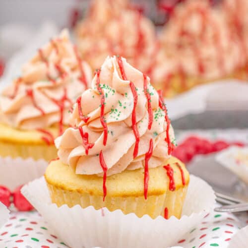 A Little Debbie Christmas Tree Cupcake with pink swirled frosting, red drizzle, and green sprinkles sits in a white paper liner on a festive napkin.