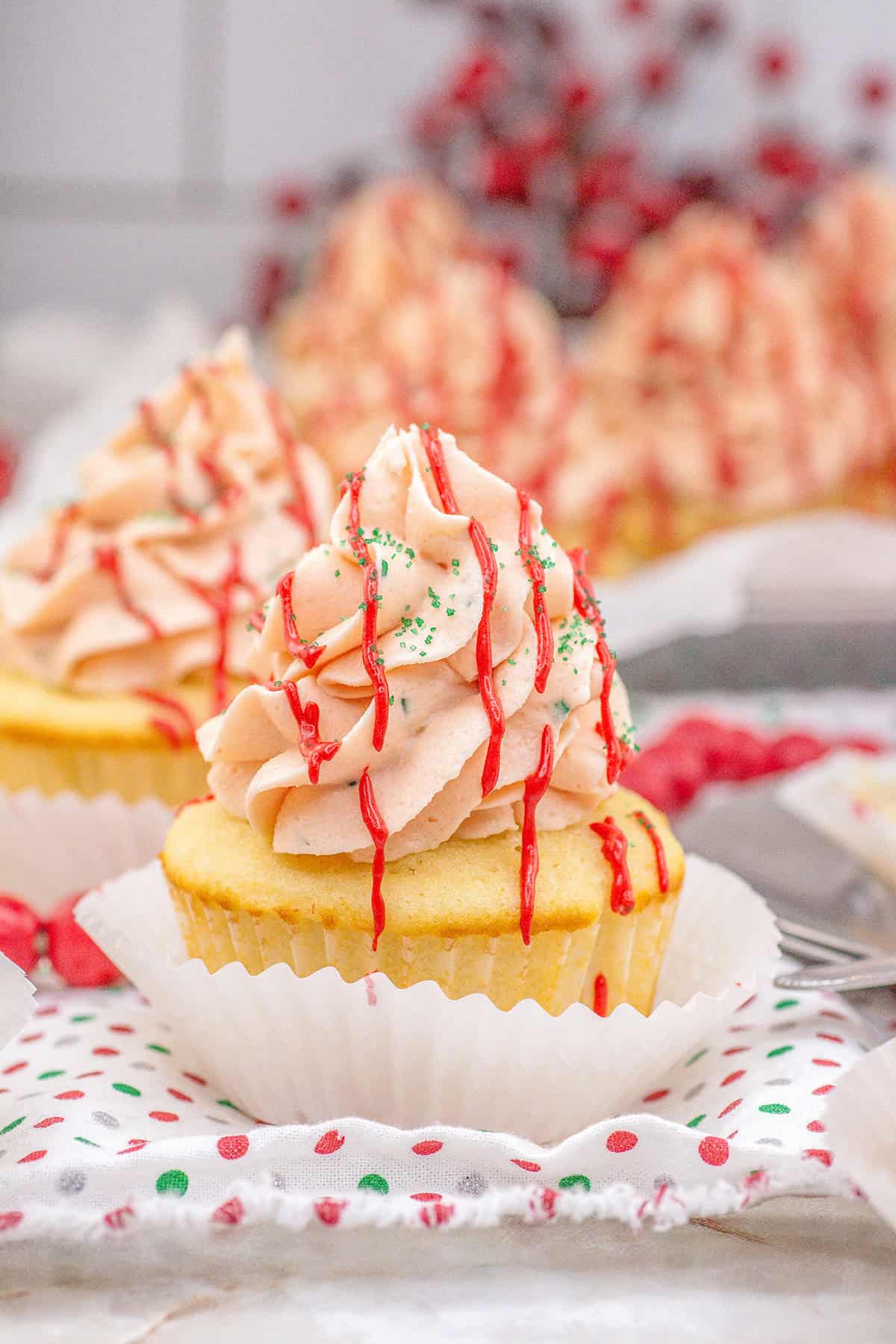 A Little Debbie Christmas Tree Cupcake with pink swirled frosting, red drizzle, and green sprinkles sits in a white paper liner on a festive napkin.