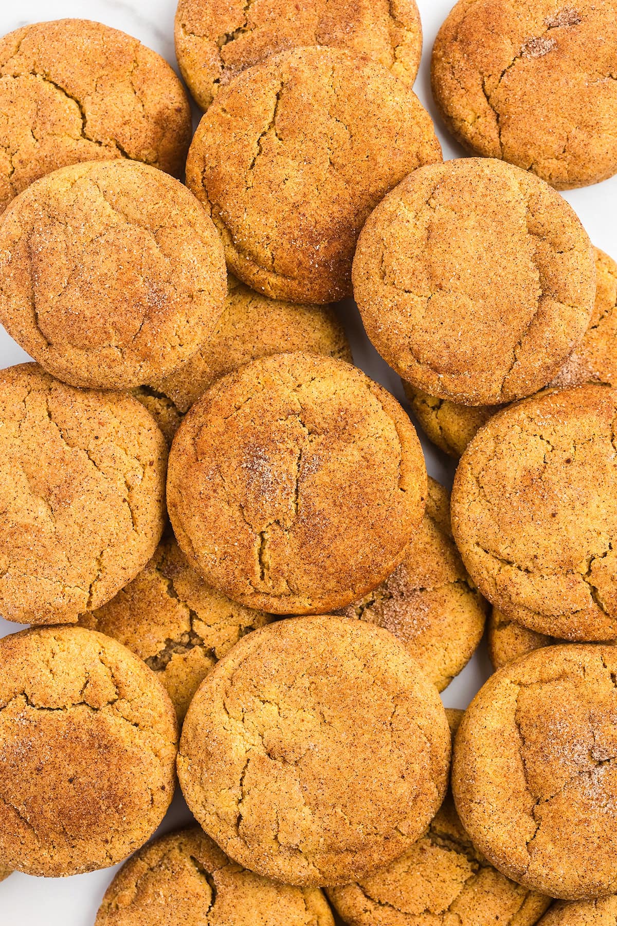 A close-up view of several round, golden-brown Pumpkin Snickerdoodles with a cracked surface, arranged in an overlapping pattern.