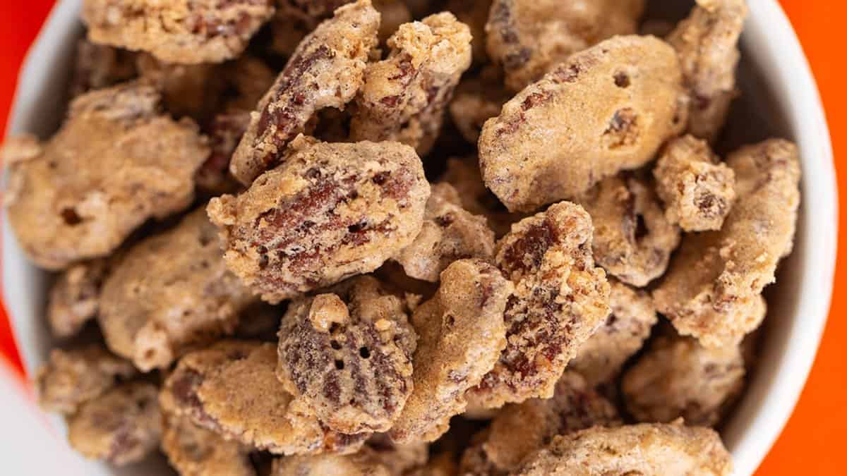 A bowl filled with candied pecans coated in a sugary, crunchy layer&mdash;perfect for adding to cookie boxes or enjoying as homemade Christmas candies.