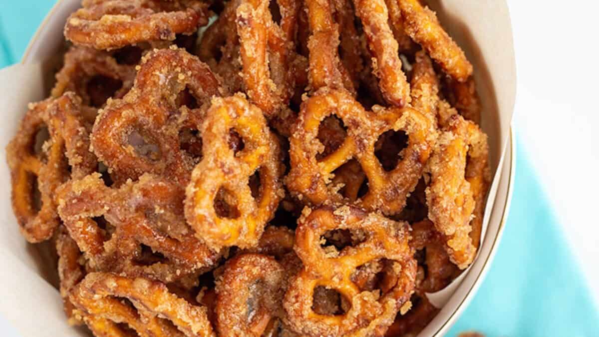 A bowl filled with small pretzels coated in a glistening cinnamon sugar mixture, perfect for adding to Christmas cookie boxes or gifting alongside homemade candies.