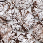 A close-up view of several Chocolate Cool Whip Cookies coated with powdered sugar and arranged on a white surface.