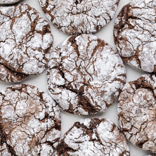 A close-up view of several Chocolate Cool Whip Cookies coated with powdered sugar and arranged on a white surface.