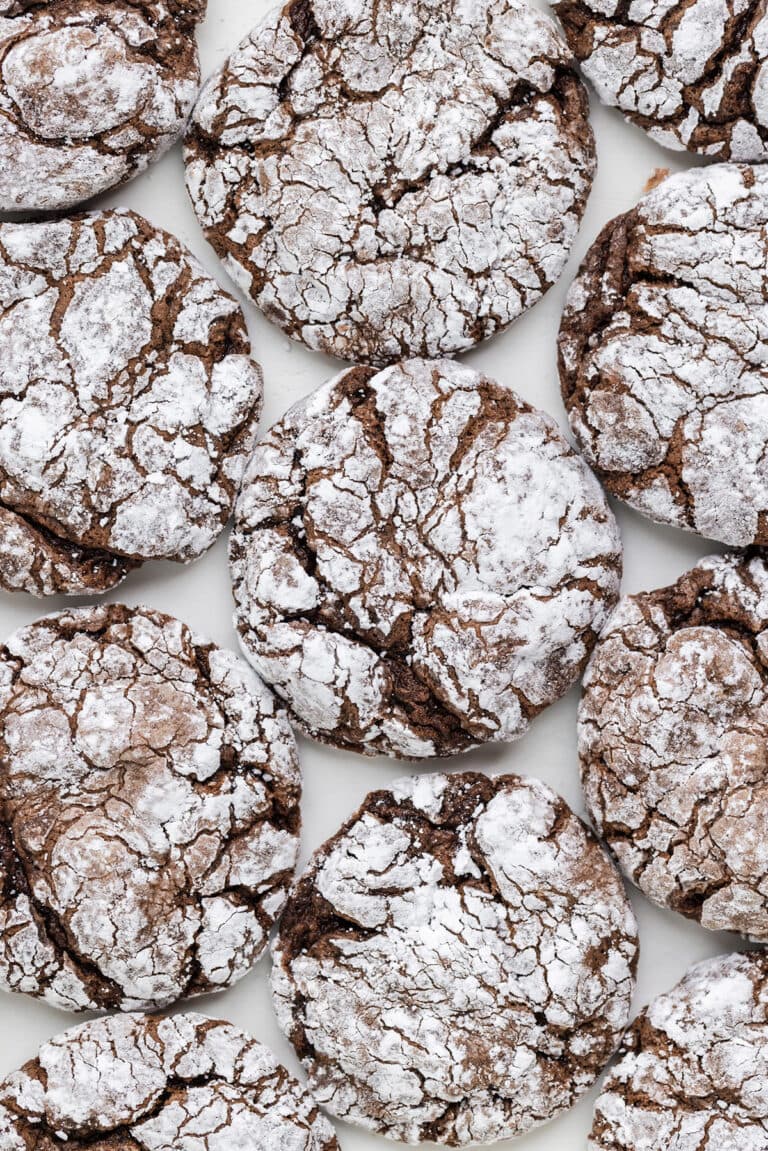 A close-up view of several Chocolate Cool Whip Cookies coated with powdered sugar and arranged on a white surface.