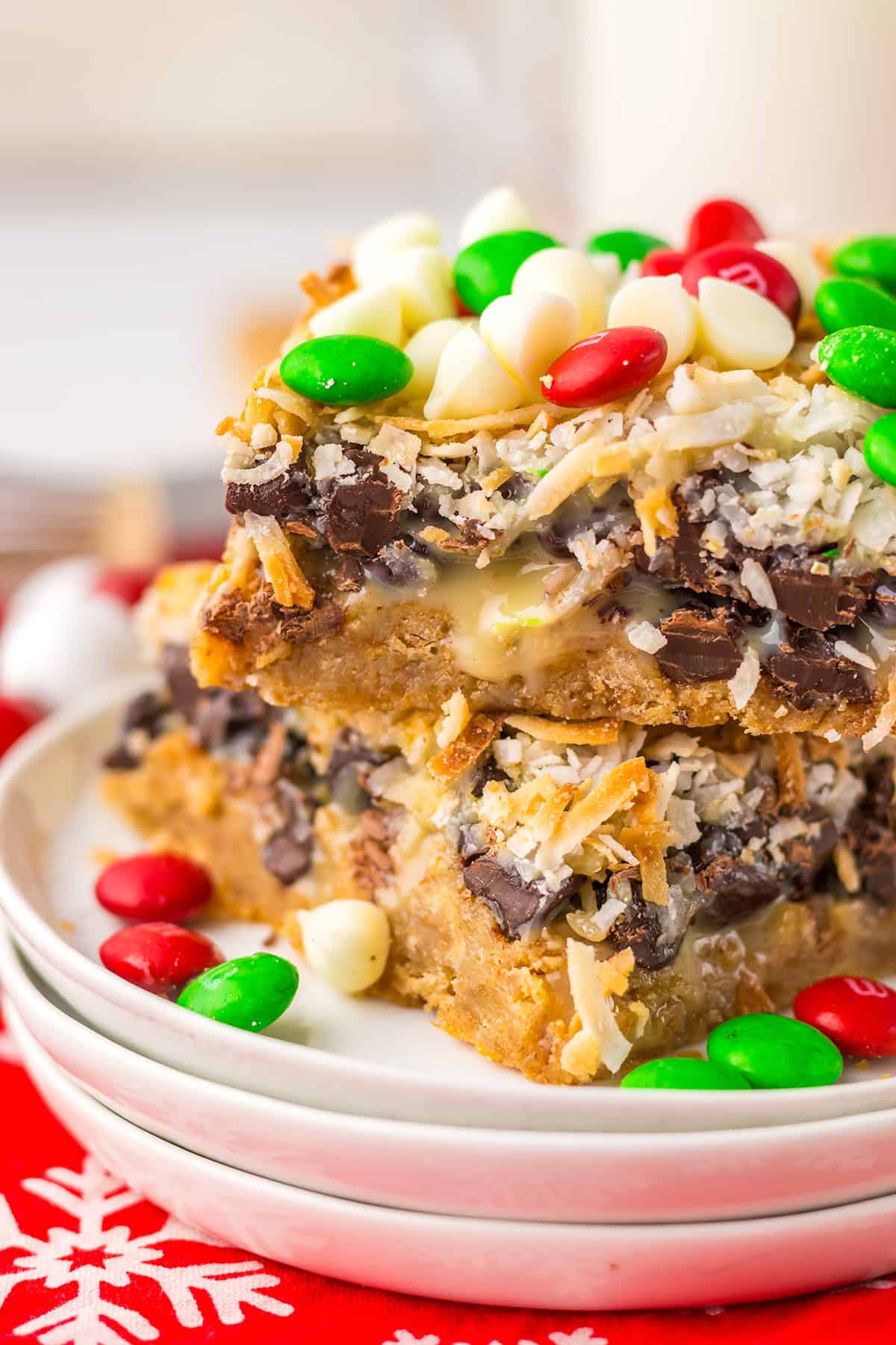 A stack of Christmas Magic Cookie Bars topped with shredded coconut, chocolate chips, and red, green, and white candies on a white plate.