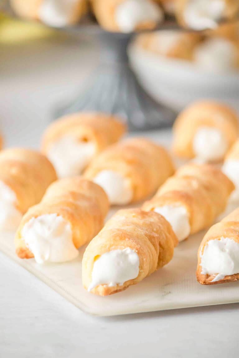 Several cream-filled Lady Locks pastry horns are arranged on a white surface, with more delicious cookies visible in the blurred background.