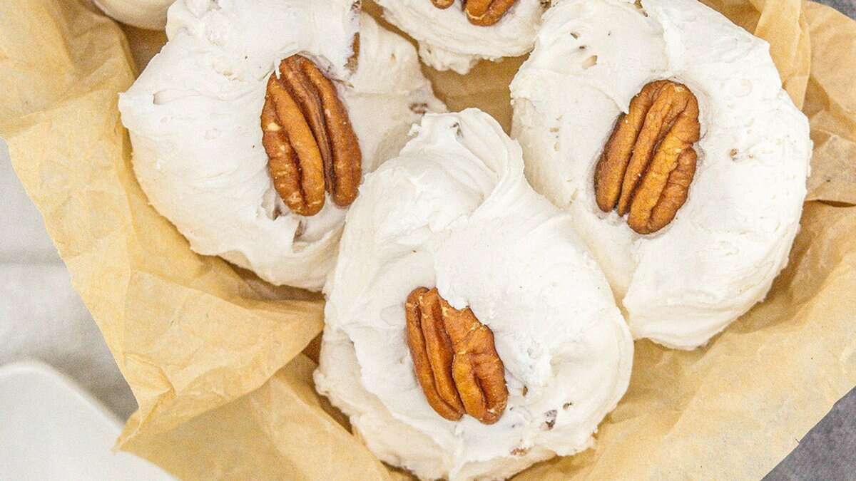 Several pieces of white divinity candy topped with pecan halves are arranged on parchment paper in a basket, making perfect homemade Christmas candies for festive cookie boxes.
