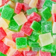 Brightly colored red, green, and yellow sugar-coated homemade gumdrops are scattered in a close-up view, perfect as festive Christmas candy.
