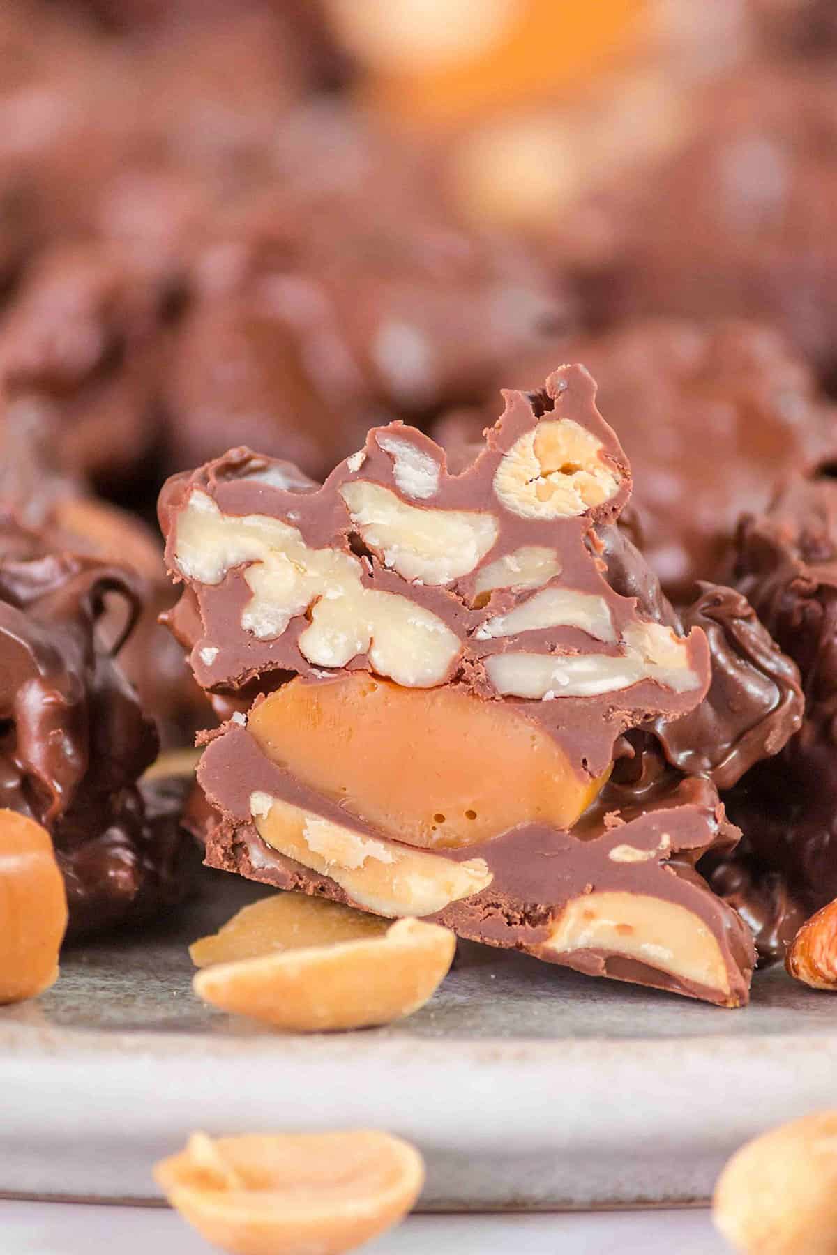 Close-up of a crockpot turtle candy cluster, revealing layers of peanuts, caramel, and chocolate coating, with scattered peanuts in the foreground.