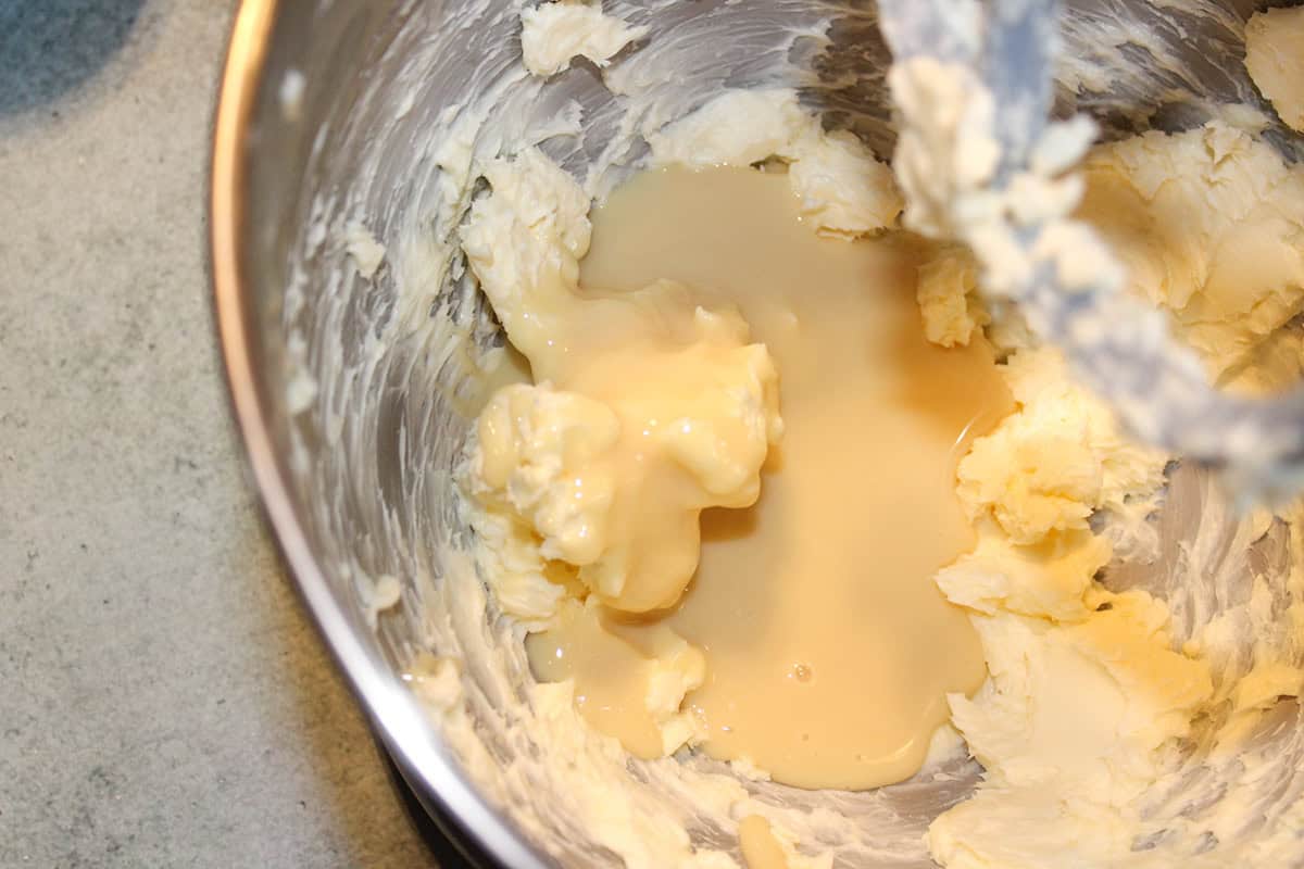 A metal mixing bowl containing creamed butter and sweetened condensed milk being mixed together, the perfect start for delicious Snowball Cookies.