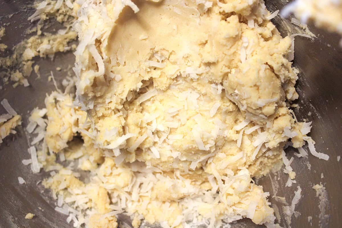 Close-up of raw cookie dough mixed with shredded coconut and sweetened condensed milk in a metal bowl, perfect for making delicious snowball cookies.