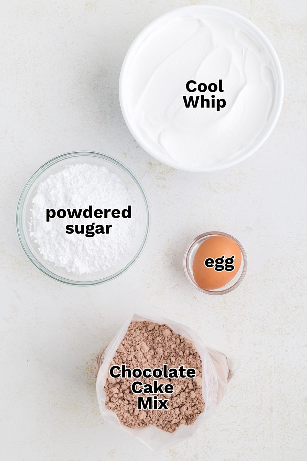 Four ingredients for Cool Whip cookies on a white surface: a bowl of Cool Whip, powdered sugar, one egg, and a bag of chocolate cake mix, each labeled with text&mdash;perfect for an easy chocolate dessert.