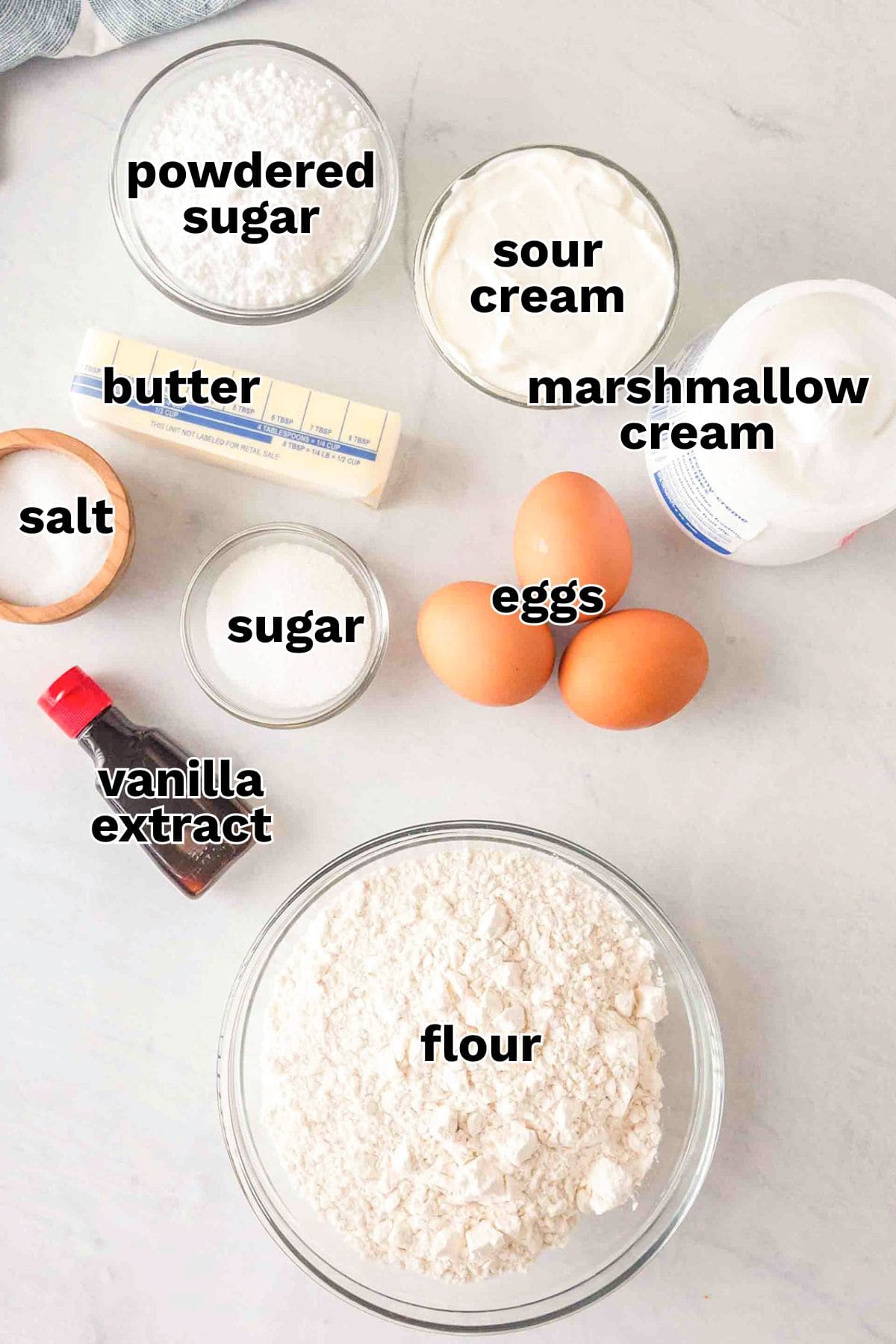 Ingredients for Lady Locks on a countertop: bowls of powdered sugar, flour, sugar, salt, sour cream, marshmallow cream, three eggs, a stick of butter, and a bottle of vanilla extract—everything you need to make classic Clothespin Cookies.