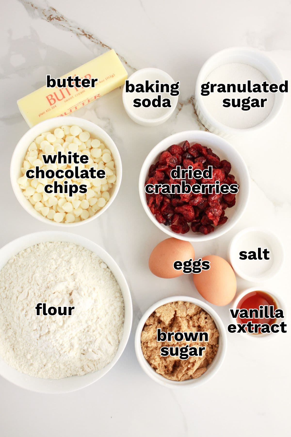 Ingredients for cranberry and white chocolate bars—including butter, white chocolate chips, dried cranberries, flour, brown sugar, granulated sugar, eggs, vanilla extract, baking soda, and salt—arranged on a countertop.