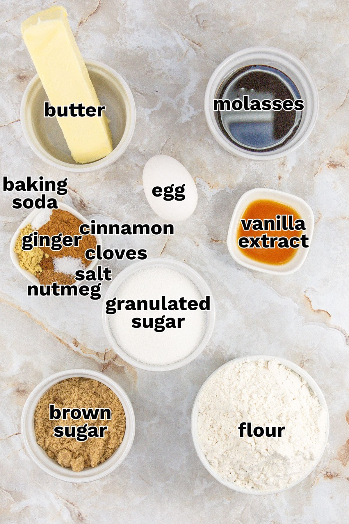Top-down view of Gingerbread Cookie Bars ingredients—butter, molasses, baking soda, egg, vanilla extract, granulated sugar, flour, brown sugar, and spices—labeled in small bowls on a marble surface.