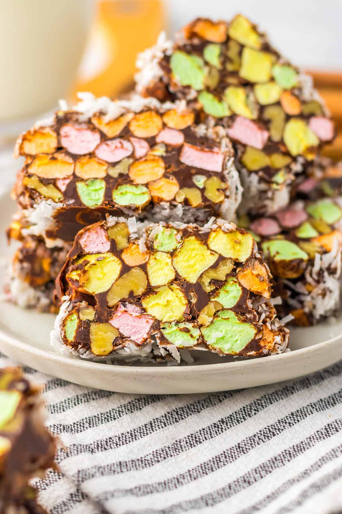 Three slices of Church Window Cookies with colorful mini marshmallows and coconut are stacked on a plate, with more no bake cookies in the background.