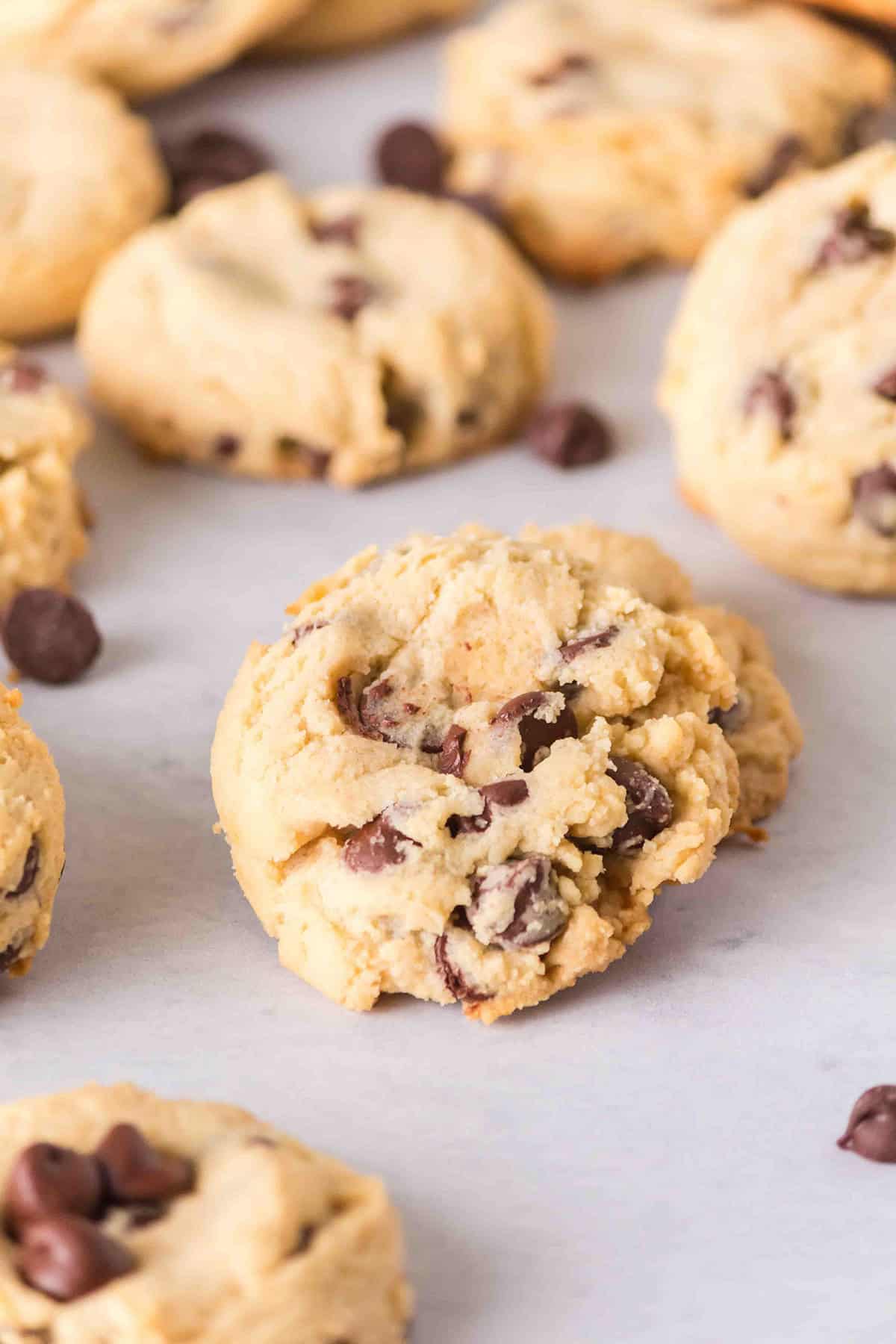 Several chocolate chip cookies, made with sweetened condensed milk, are arranged on a white surface, with visible chocolate chips throughout the cookies.