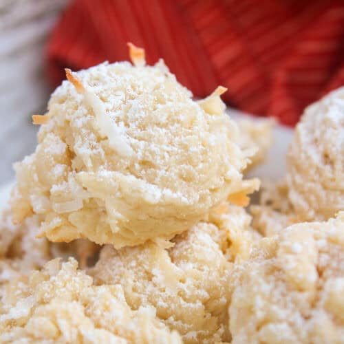 Close-up of coconut macaroons made with sweetened condensed milk and dusted with powdered sugar, with a red cloth in the background.