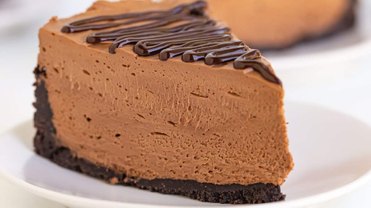 A slice of chocolate cheesecake with a chocolate cookie crust and chocolate drizzle on top, served on a white plate&mdash;a true delight for fans of decadent desserts and classic chocolate recipes.
