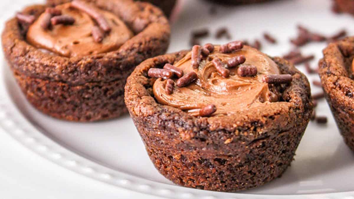 Close-up of decadent chocolate cookie cups filled with rich chocolate frosting and topped with chocolate sprinkles, arranged on a white plate&mdash;perfect for lovers of chocolate desserts.