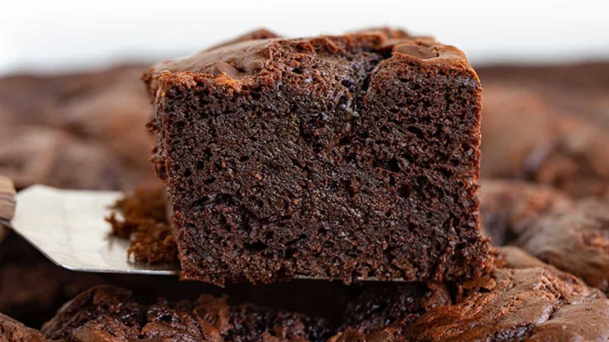 A close-up of a thick, moist chocolate brownie on a spatula, with more brownies in the background&mdash;perfect for anyone who loves decadent chocolate desserts.