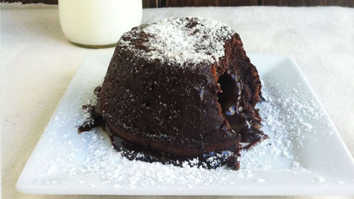 A chocolate lava cake with a gooey center sits on a white plate, dusted with powdered sugar&mdash;a standout among decadent desserts&mdash;with a glass of milk in the background.