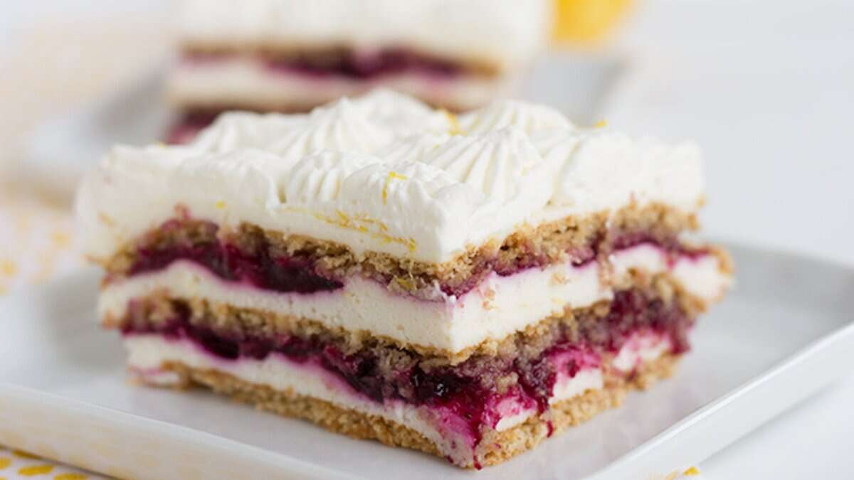 A slice of layered dessert with whipped cream, berry filling, and cake or biscuit layers is served on a white plate—perfect for those who love refreshing spring desserts.