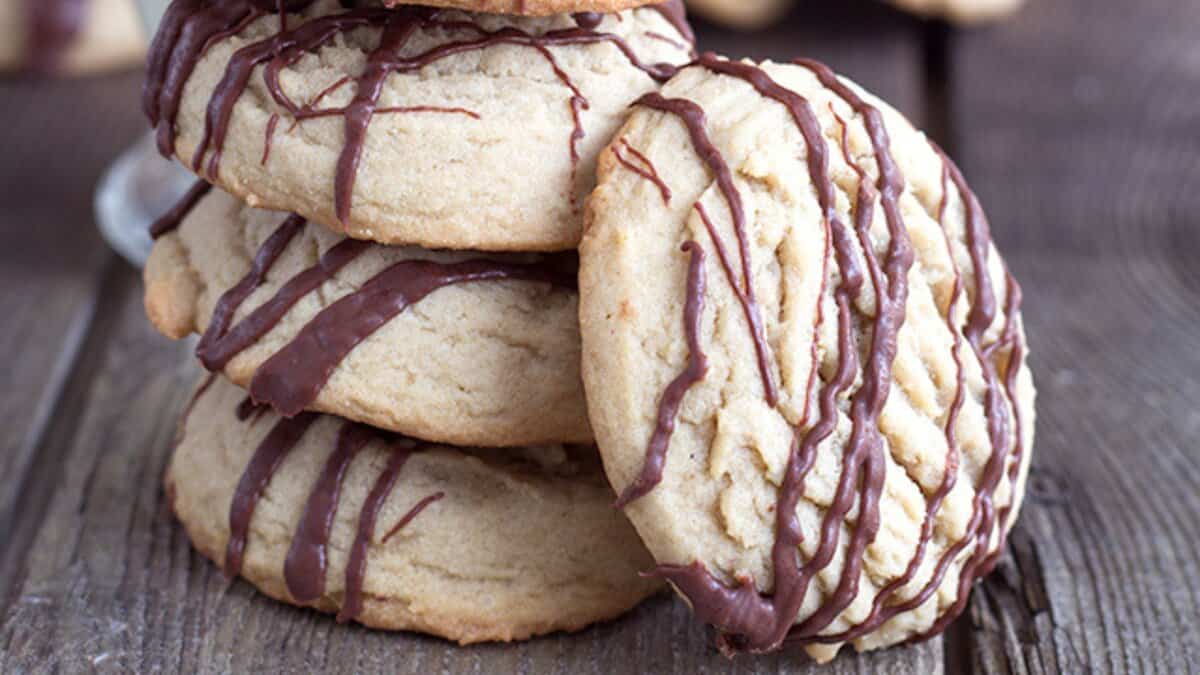 A stack of thick, round cookies drizzled with chocolate sits on a wooden surface&mdash;perfect inspiration for easy cookie recipes using pantry staples.