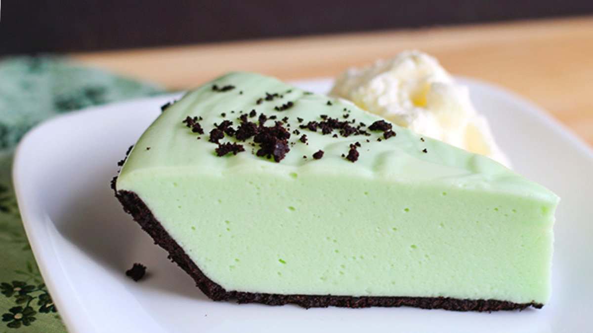 A slice of light green pie with a chocolate cookie crust on a white plate, topped with chocolate crumbs and a dollop of whipped cream—perfect for lovers of mint chocolate desserts or as a festive St. Patrick's Day treat.