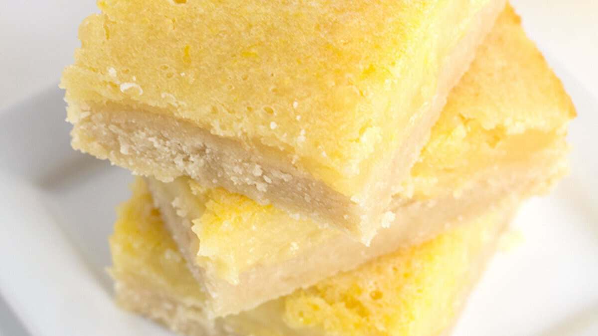 Three square lemon bars stacked on a white plate, showing a light yellow, creamy filling with a slightly browned top and crumbly edges—perfect for anyone who loves refreshing lemon desserts or easy spring desserts.