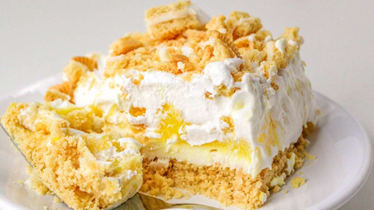 A slice of layered dessert with a crumbly cookie crust, creamy filling, whipped topping, and crumbled cookies on a white plate—perfect for fans of lemon desserts and refreshing spring desserts.