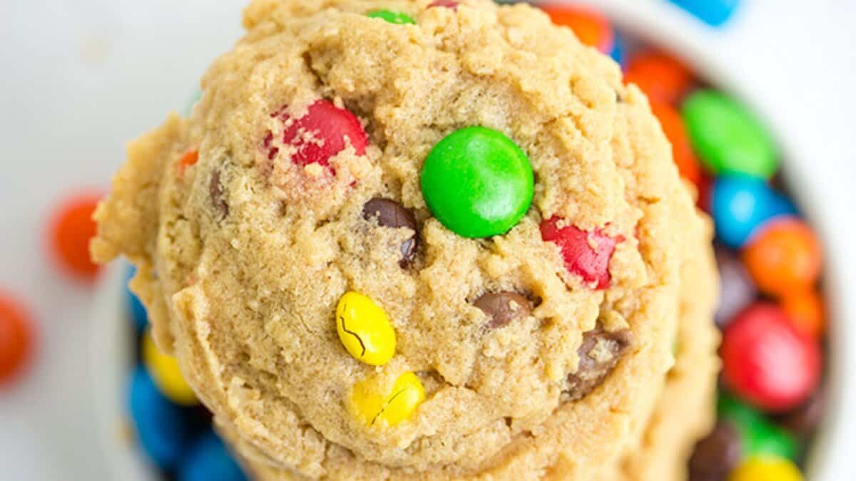 A close-up of a cookie with colorful candy-coated chocolates and chocolate chips on top, with more candies in the background&mdash;perfect inspiration for your easy cookie recipes using pantry staples.