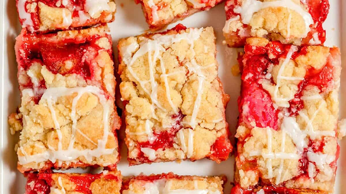 Nine rectangular strawberry crumb bars with white icing drizzle are arranged on a white surface, making them the perfect spring desserts for anyone who loves fresh strawberry recipes.