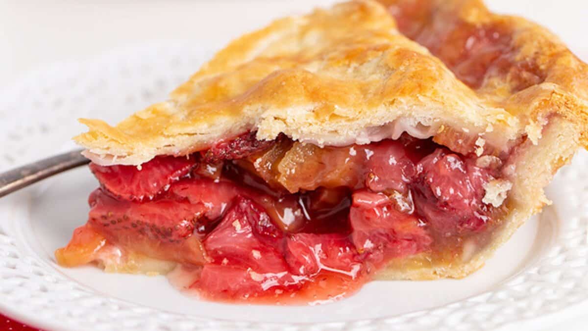 A slice of strawberry rhubarb pie on a white plate, showing a golden crust and juicy red filling—a classic spring strawberry dessert made with fresh strawberries.