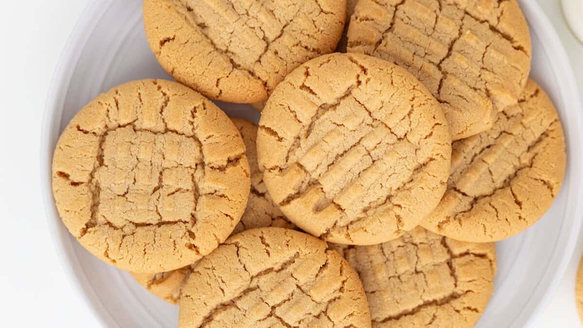 A white plate filled with round peanut butter cookies, made from pantry staples and showing characteristic crisscross fork marks on their tops&mdash;perfect for anyone seeking easy cookie recipes.