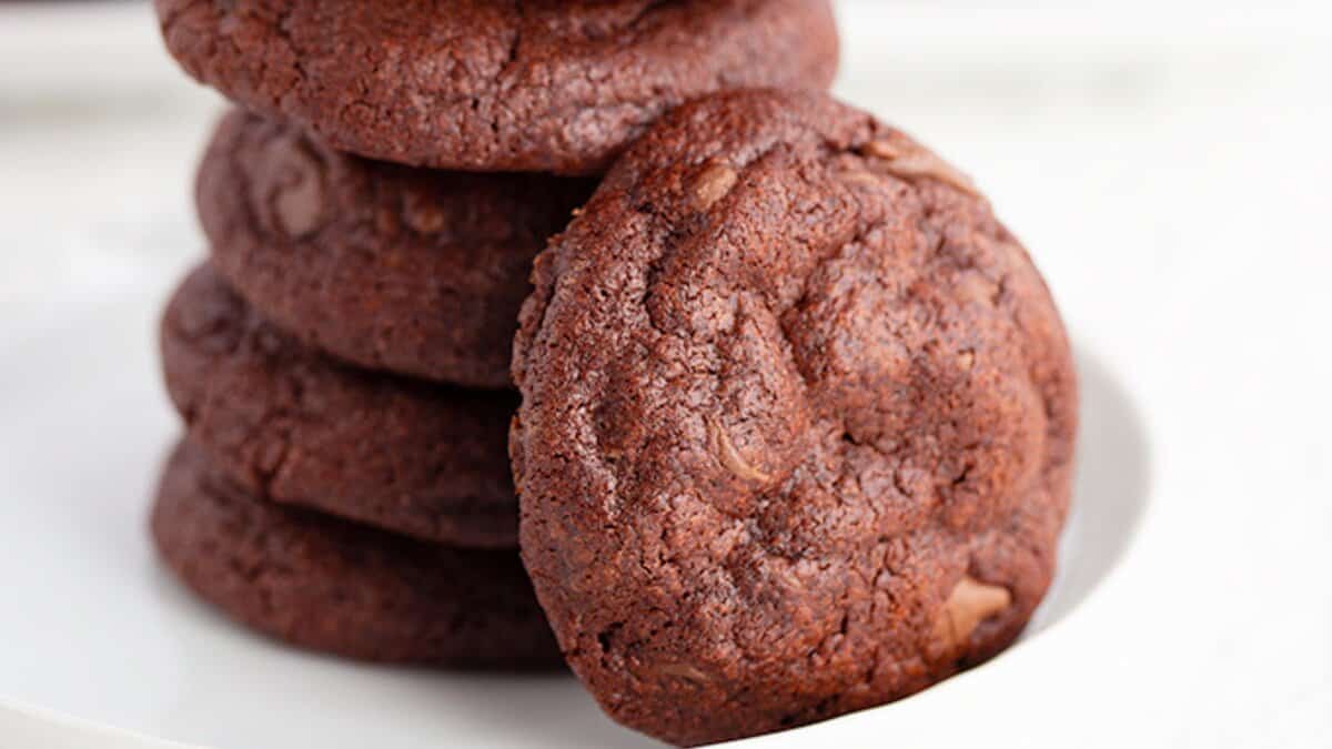 A stack of chocolate cookies, made with pantry staples, is arranged on a white plate, with one cookie leaning against the stack.