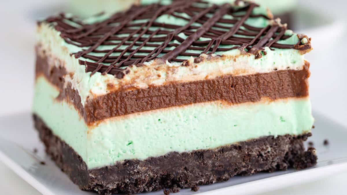 A layered Mint Chocolate dessert bar with a chocolate cookie base, two layers of mint and chocolate cream, topped with a rich chocolate drizzle—perfect for Mint Chocolate Desserts or St. Patrick’s Day treats.