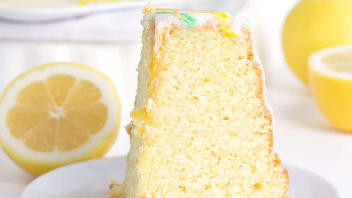 A slice of lemon cake with white icing on a plate, accompanied by a halved lemon and a whole lemon in the background—perfect for those who love spring desserts or crave refreshing lemon recipes.