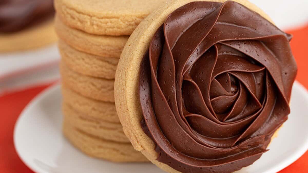 A stack of sugar cookies on a plate, with the front cookie decorated with chocolate frosting in a rose pattern&mdash;perfect for anyone seeking easy cookie recipes using simple pantry staples.