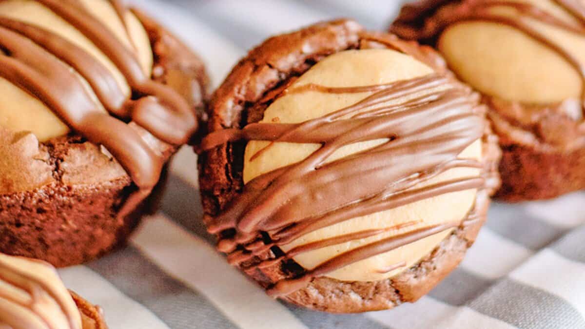 Close-up of chocolate brownie cups topped with a round peanut butter filling and drizzled with chocolate—perfect mini desserts for spring parties, displayed on a striped cloth.