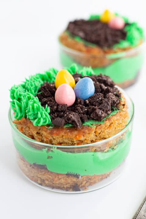 A dessert cup with green frosting, crumbled chocolate cookies resembling soil, and three candy eggs on top, this Mini Easter Trifle is perfectly decorated to look like a bird's nest—an adorable addition to your Easter desserts table.